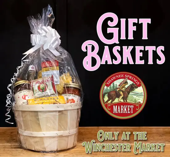 Gift basket wrapped in cellophane with various items, promoting Shawnee Springs Market, displayed at Winchester Market. Large pink and green text.