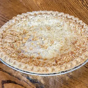 A freshly baked apple crumb pie rests on a wooden table, featuring a golden-brown crust with crumbly topping and a decorative edge.