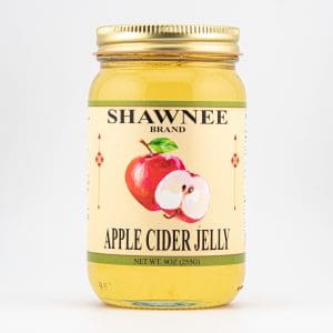 A jar of Shawnee Brand Apple Cider Jelly with a golden lid, featuring a vibrant apple illustration on the label.