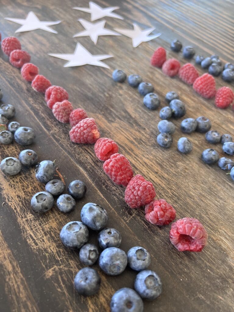 Raspberries and blueberries arranged with paper stars on a wooden surface, forming the letters "USA" in a patriotic-themed display.